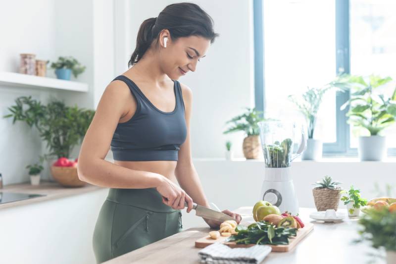 Woman in workout clothes chopping fruits.