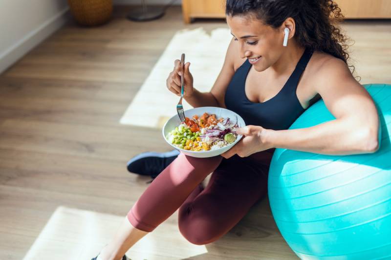 Woman eating salad next to an exercise ball.