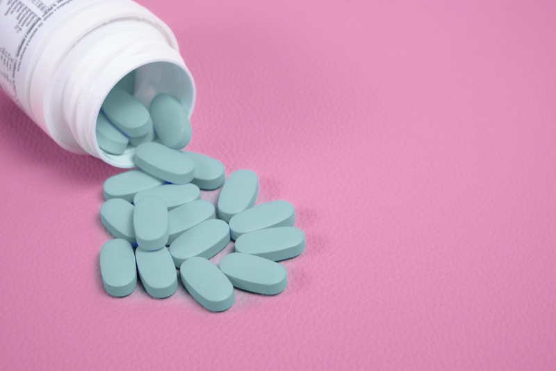 Blue pills spilling from bottle on pink surface.