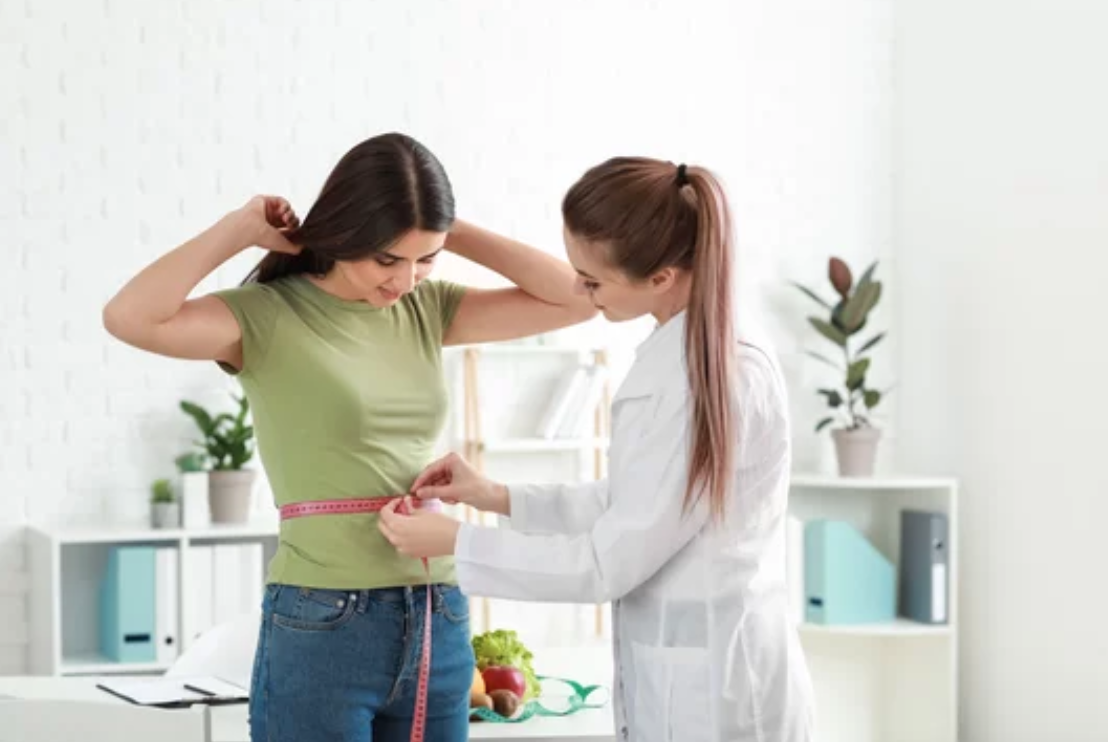 Woman measuring another woman's waist with a tape.