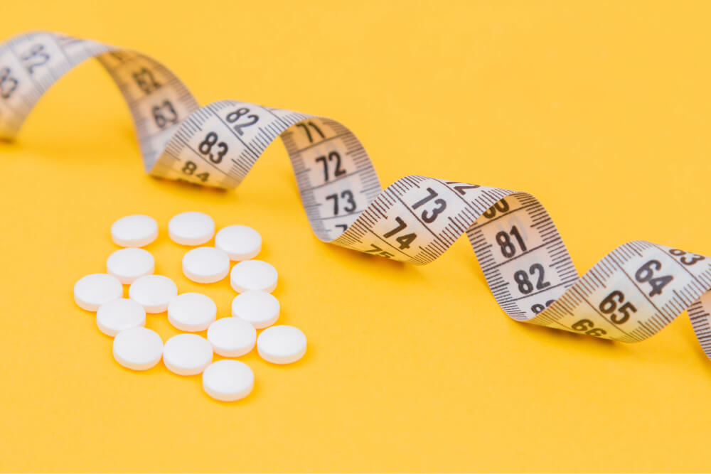 Measuring tape and round white pills on yellow background.
