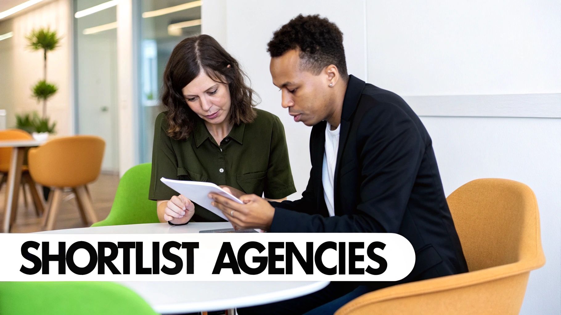 Two professionals, a man and a woman, collaborate while looking at a document at a table in an office.