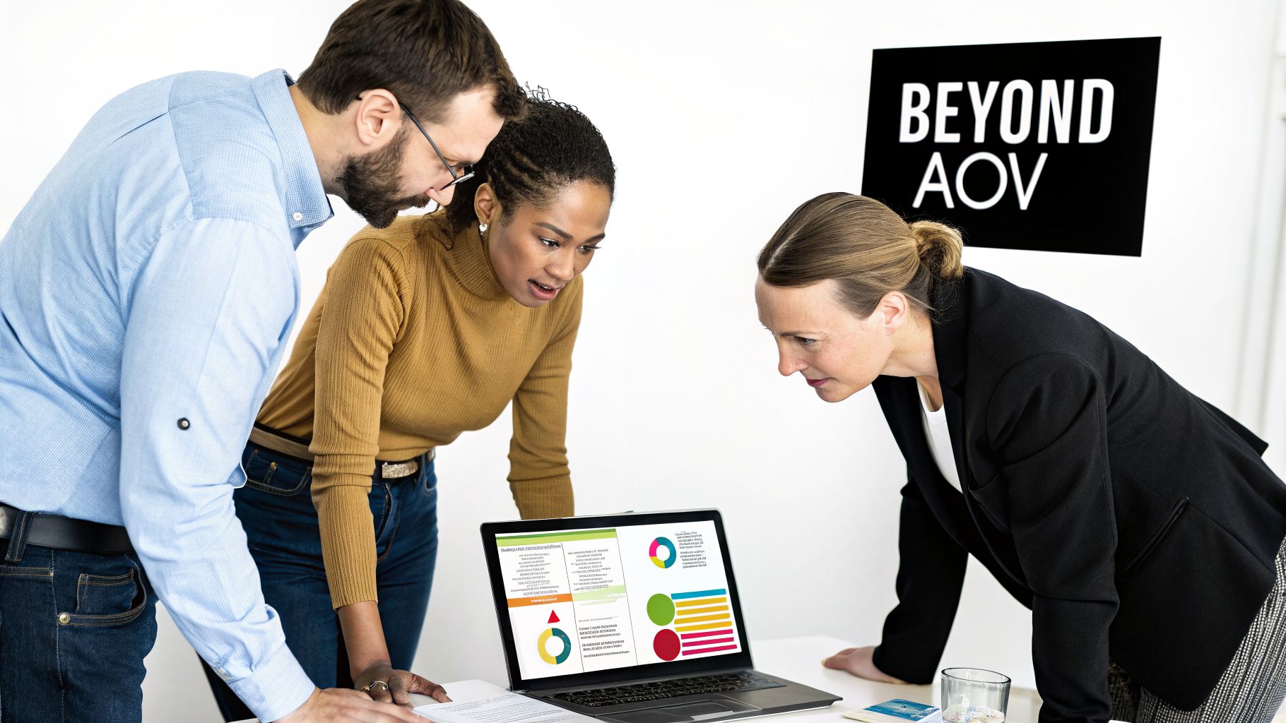 Three diverse business professionals intently reviewing data and charts on a laptop screen during a meeting.
