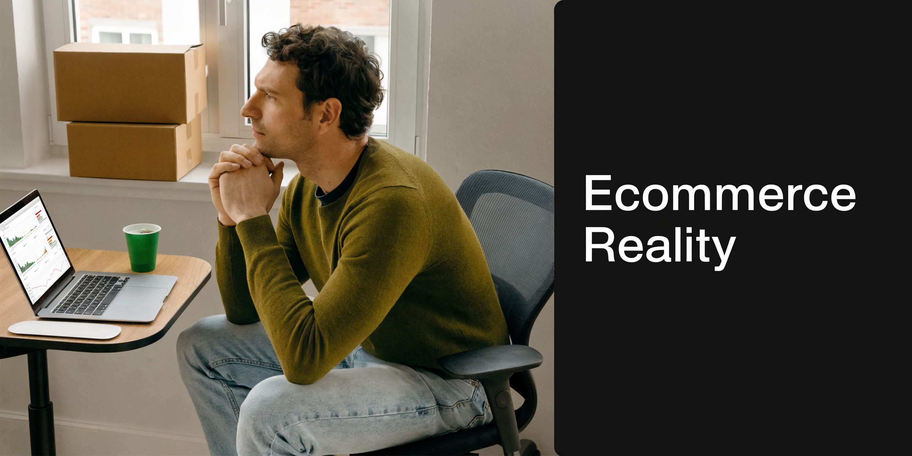 A contemplative man sitting at a desk with a laptop and shipping boxes in a modern office.