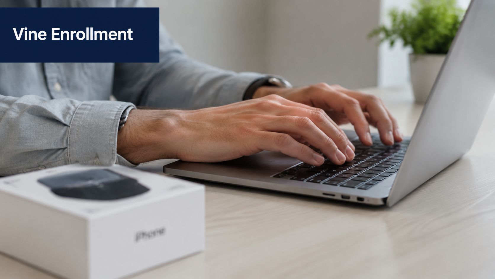 A person wearing a grey shirt is typing on a laptop with an iPhone box nearby.