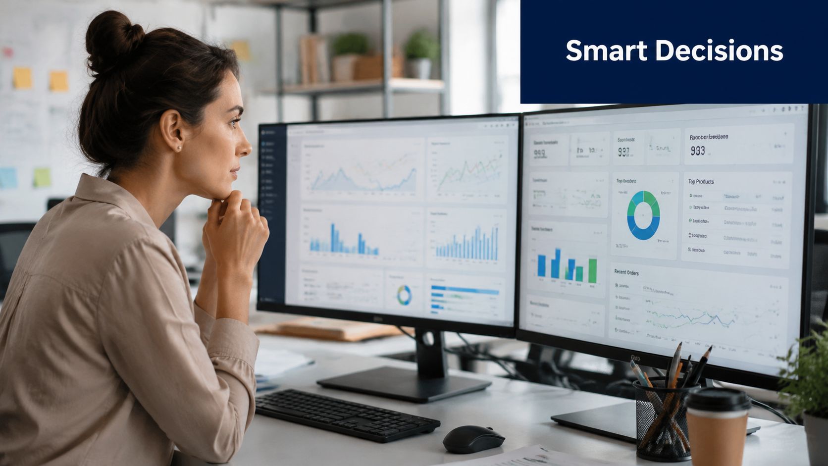 A professional woman analyzing data dashboards on two computer screens in a modern office workspace.