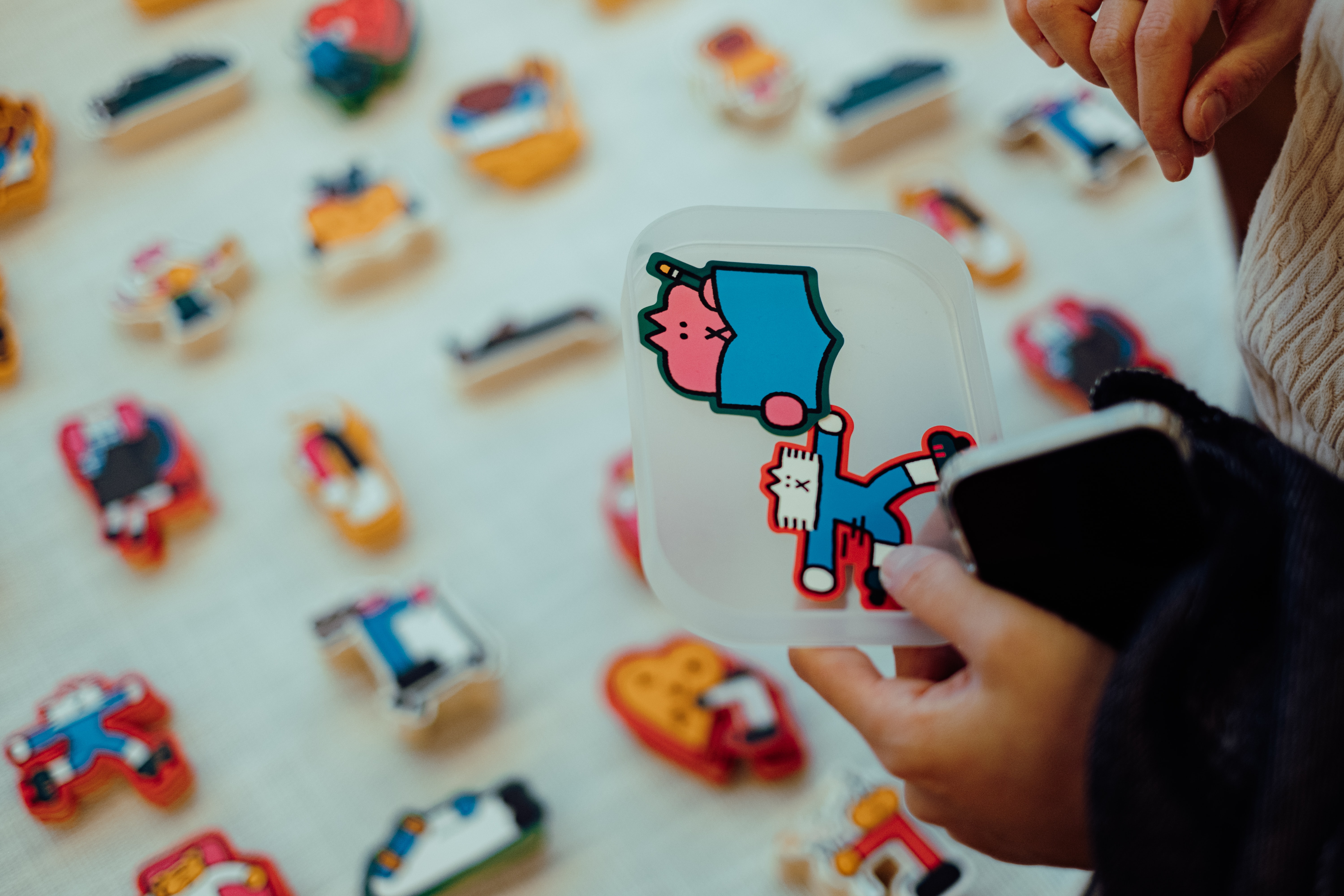 person holding a tray  with some stickets in it, and a table with stacks of stickers they are selecting form, but blured out