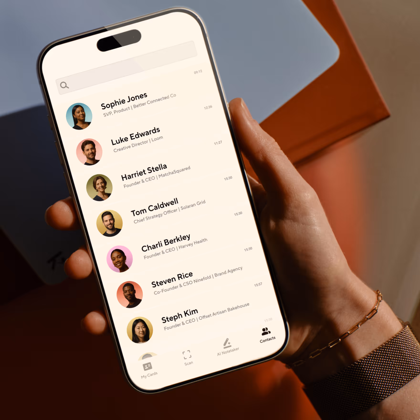 Hand holding a smartphone displaying a contacts app with profile photos and names.