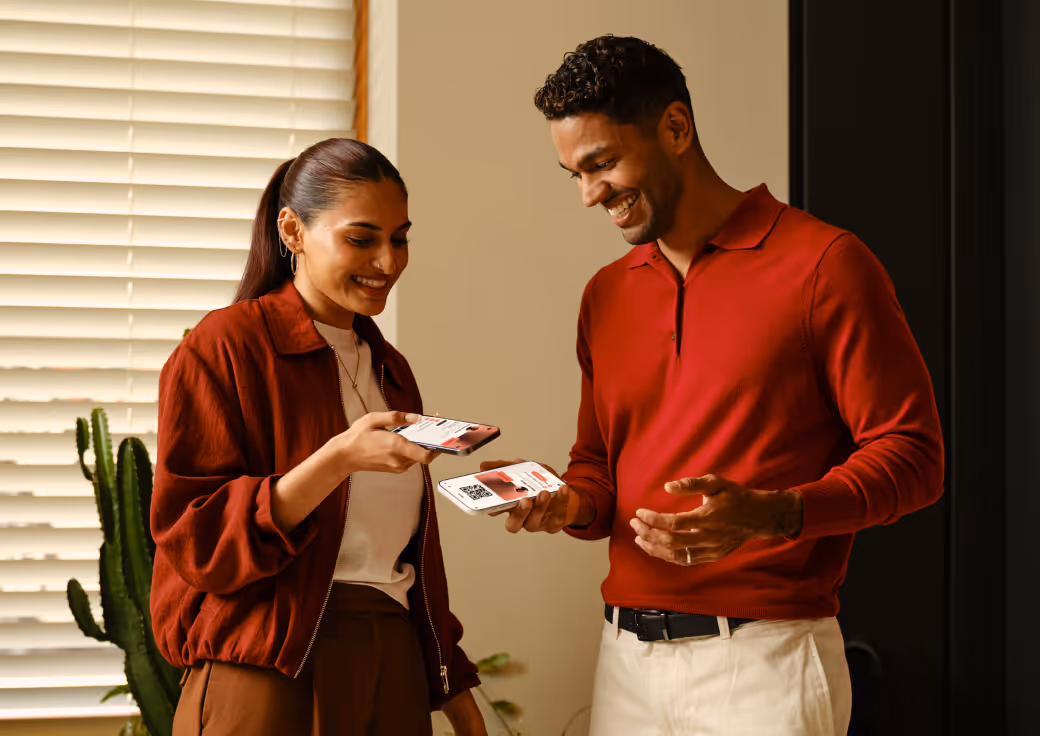 Smiling man and woman exchanging digital business cards on smartphones indoors.