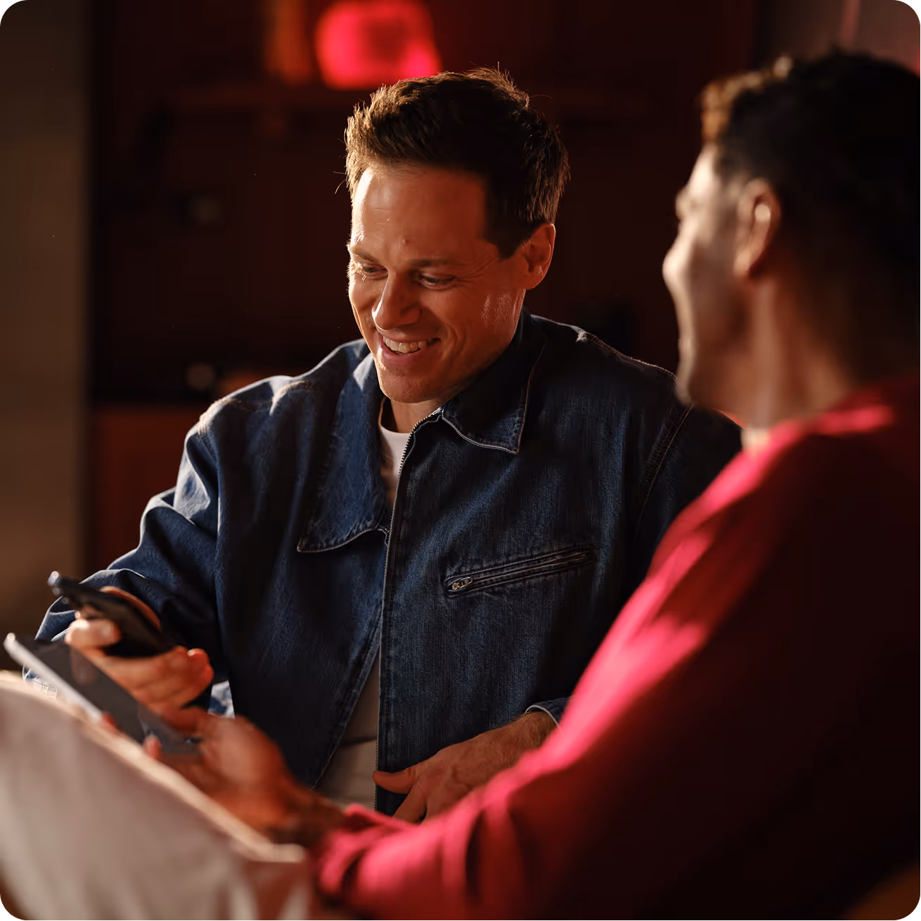 Two men smiling while sharing contact information on a smartphone at a networking event.