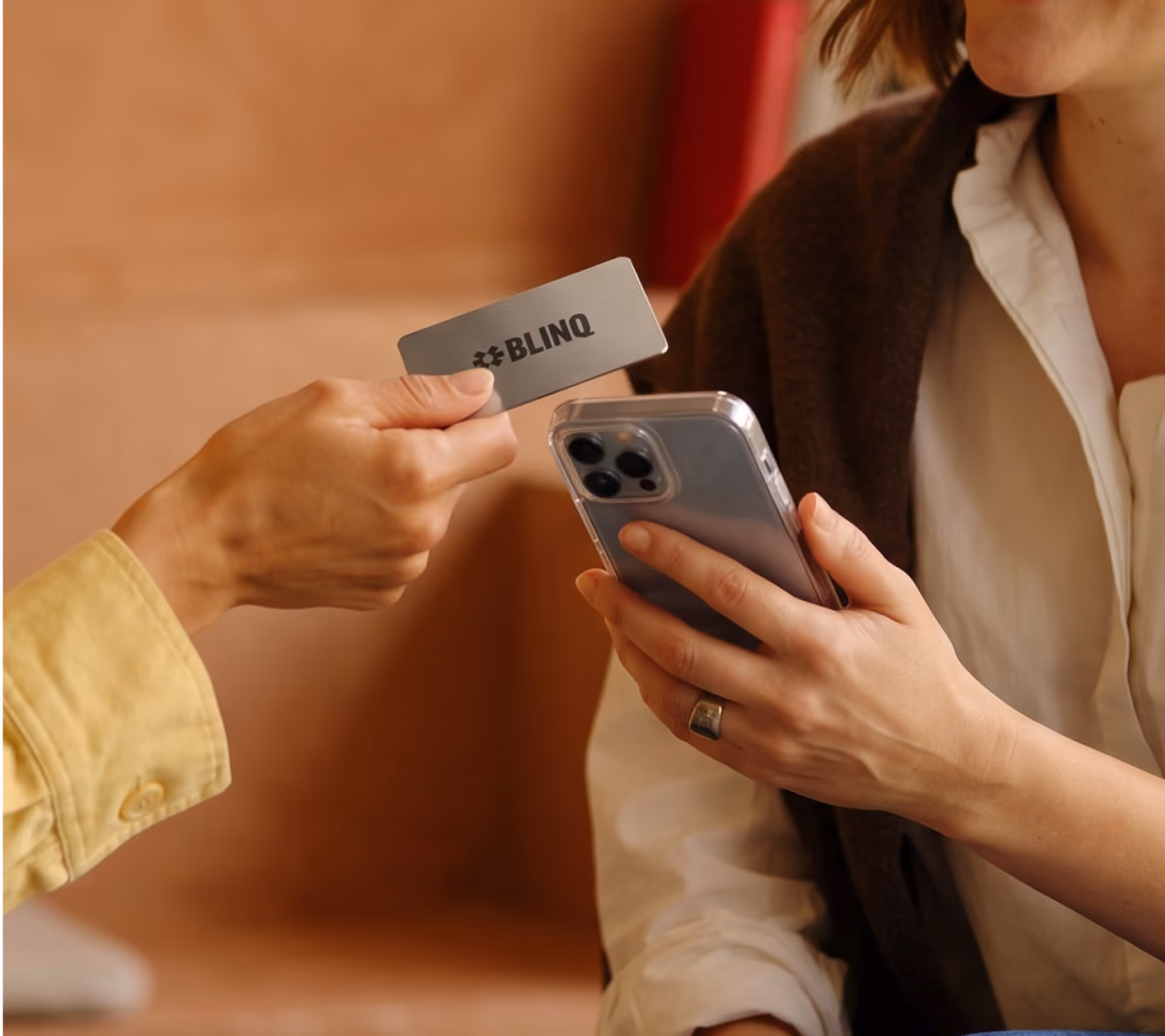 A person tapping a black metal Blinq NFC business card against the back of an iPhone to share their contact details