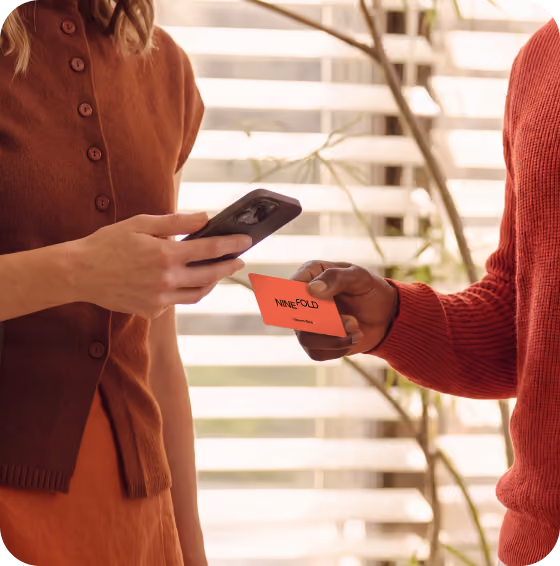 Two colleagues sharing contact details indoors, one tapping a Blinq NFC card against the other's phone