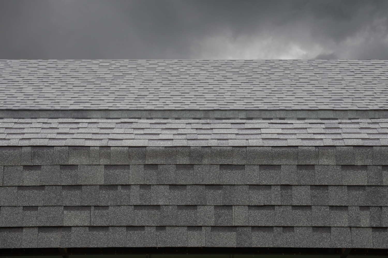 Newly installed asphalt shingles on a roof under a dark, cloudy sky.