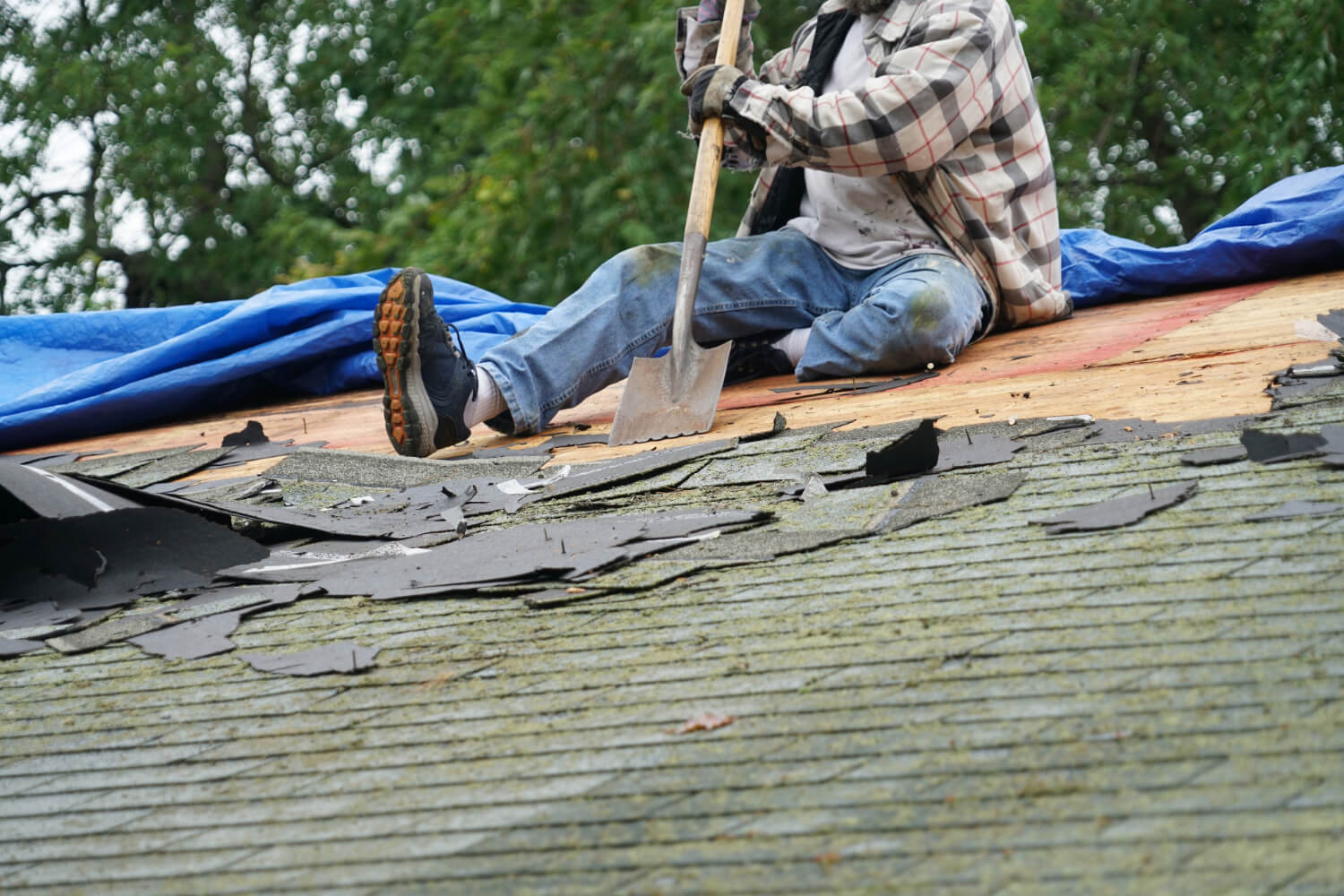 Roofer removing shingles on roof.