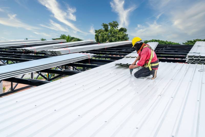 Roofer installing white metal sheets on roof.