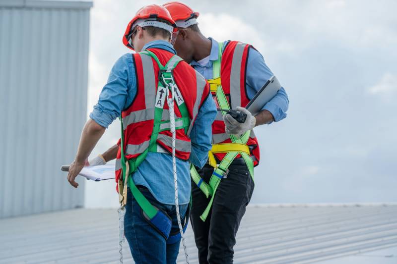 Two roofers with helmets and vests on a metal roof.