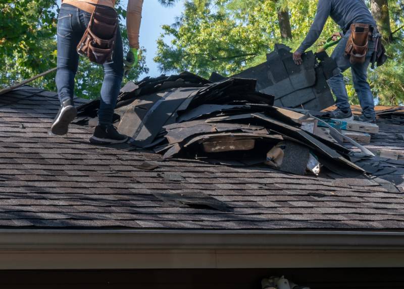 Workers removing old shingles from roof.