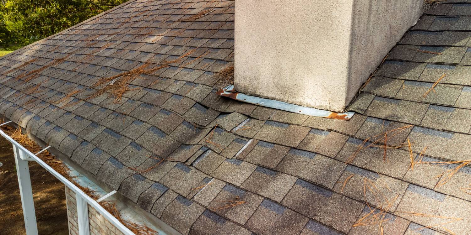 Damaged shingle roof with chimney.