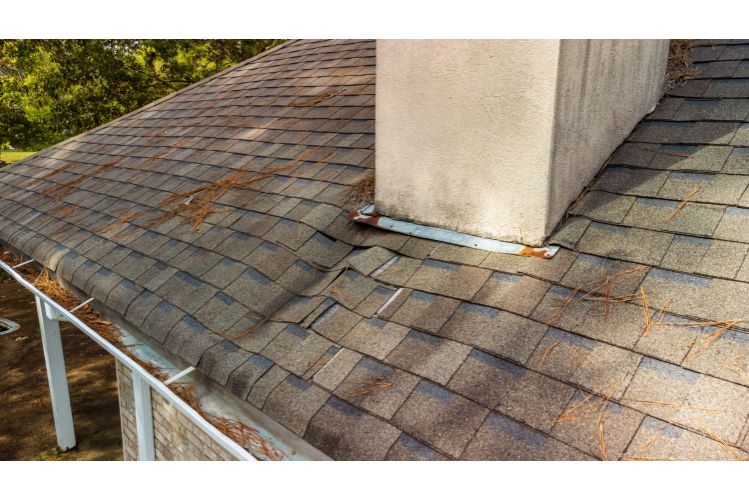 Worn roof with damaged shingles near a chimney.