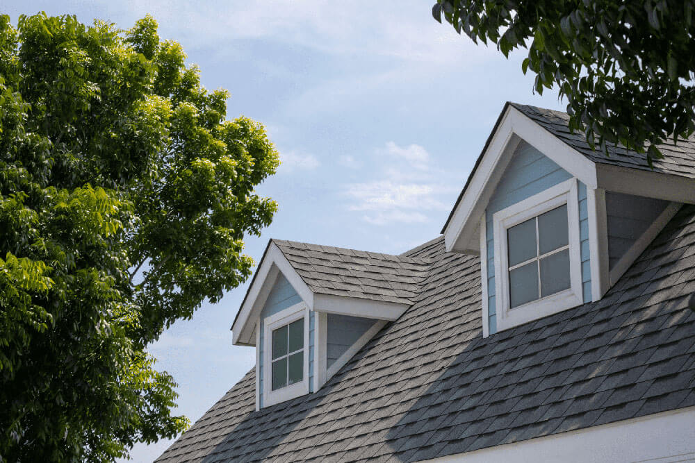 A house roof with grey shingles and two dormer windows.