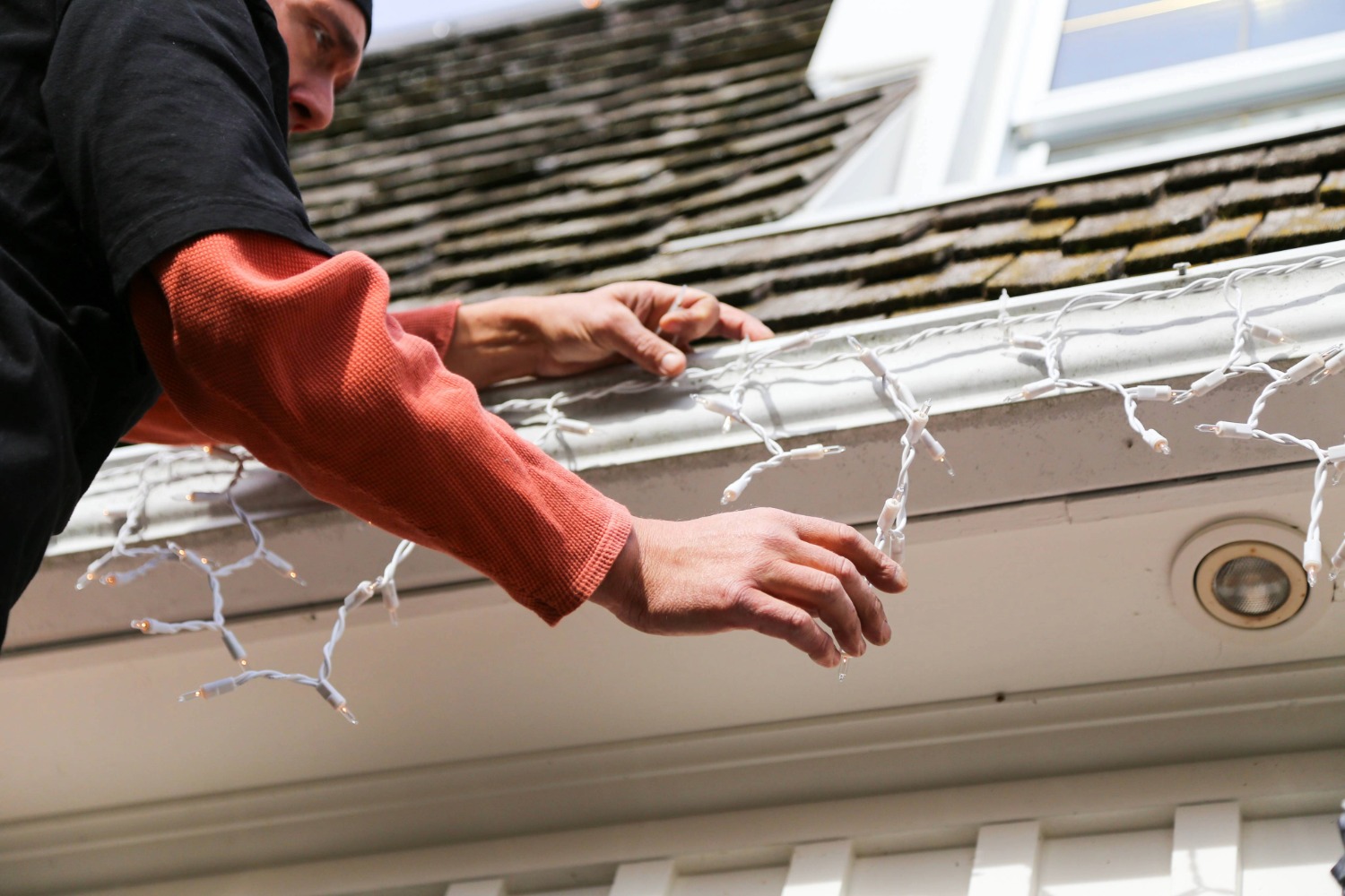 Person hanging lights on a house roof.