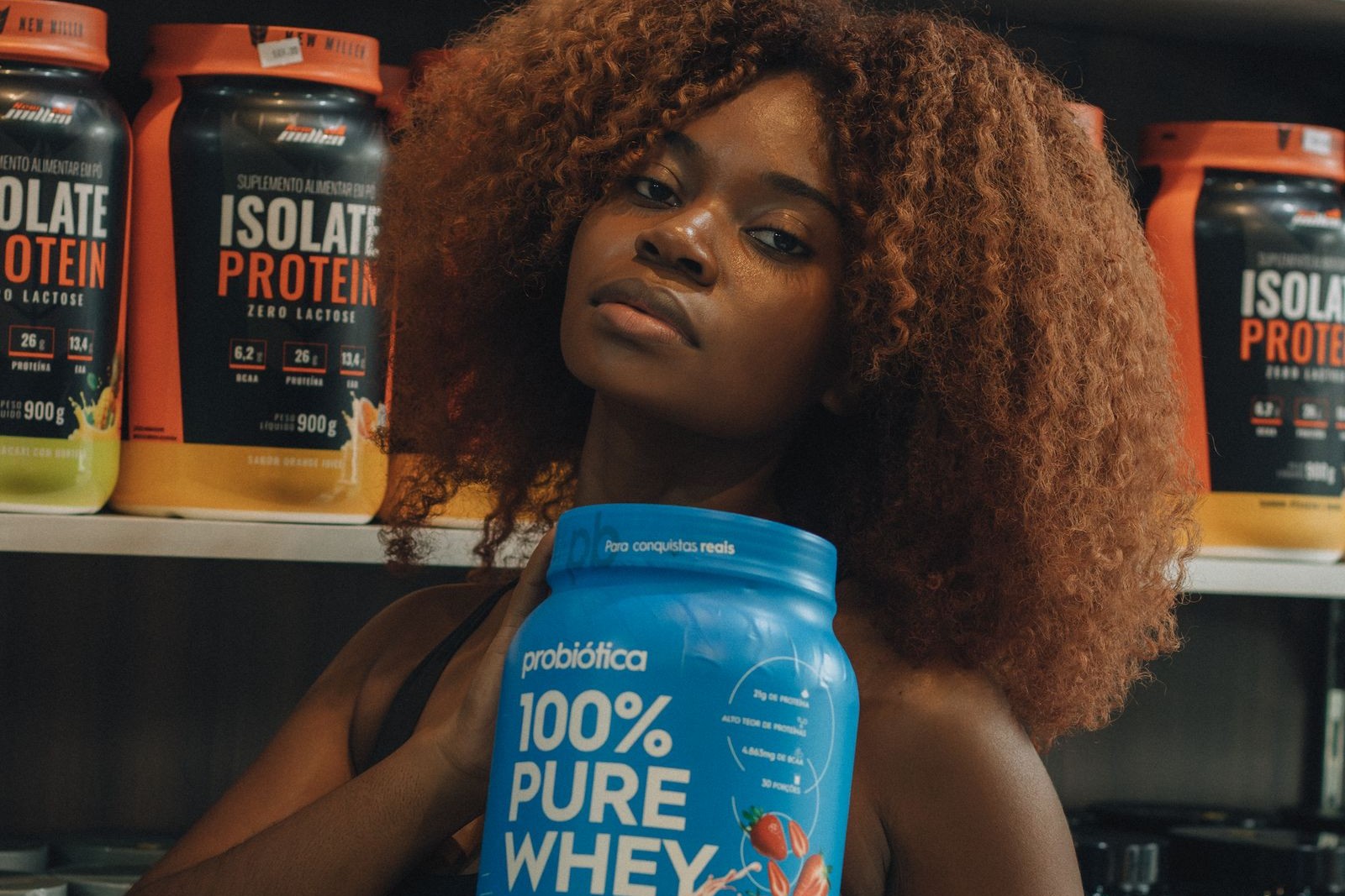 A shopper holding a tub of whey protein in front of shelves of competing sports nutrition brands