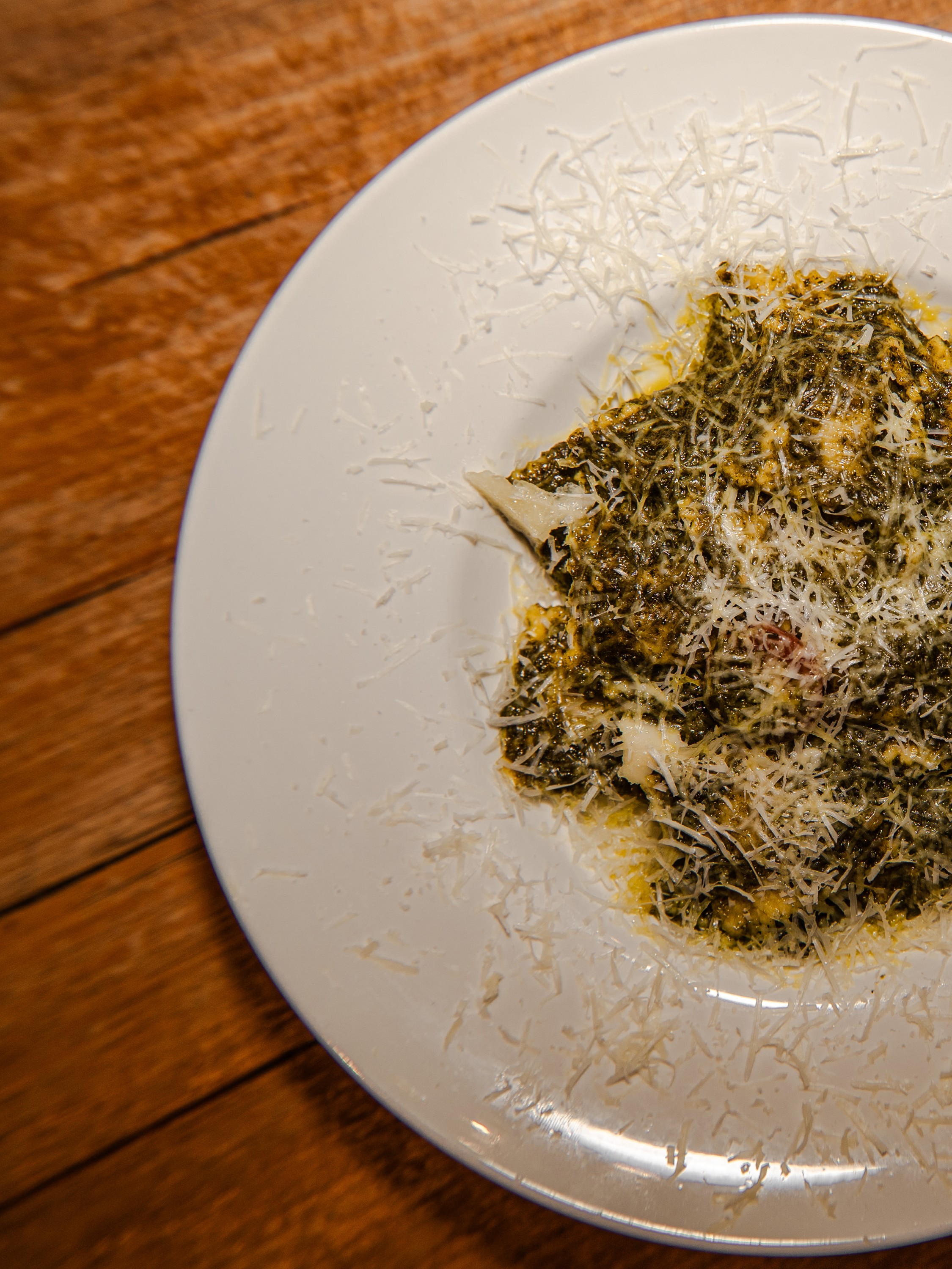 Plate of pasta coated in green pesto sauce and topped with grated parmesan cheese.