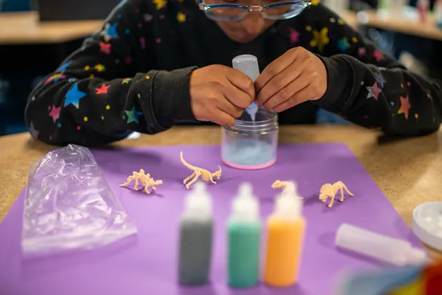 A young girl is doing crafts on a table.