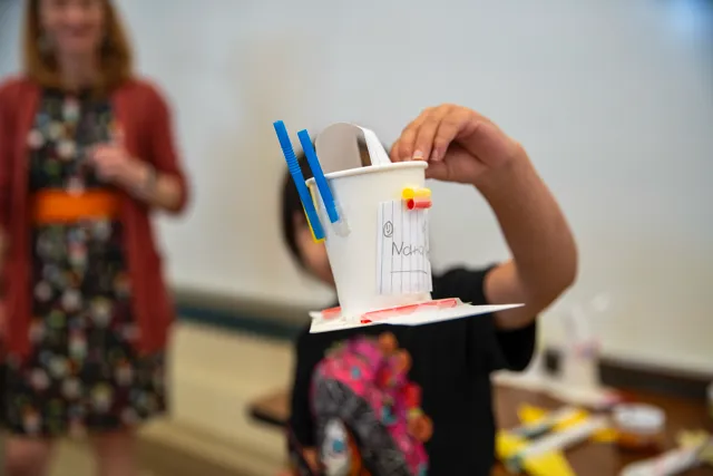 A young boy holding a cup with toothbrushes in it.