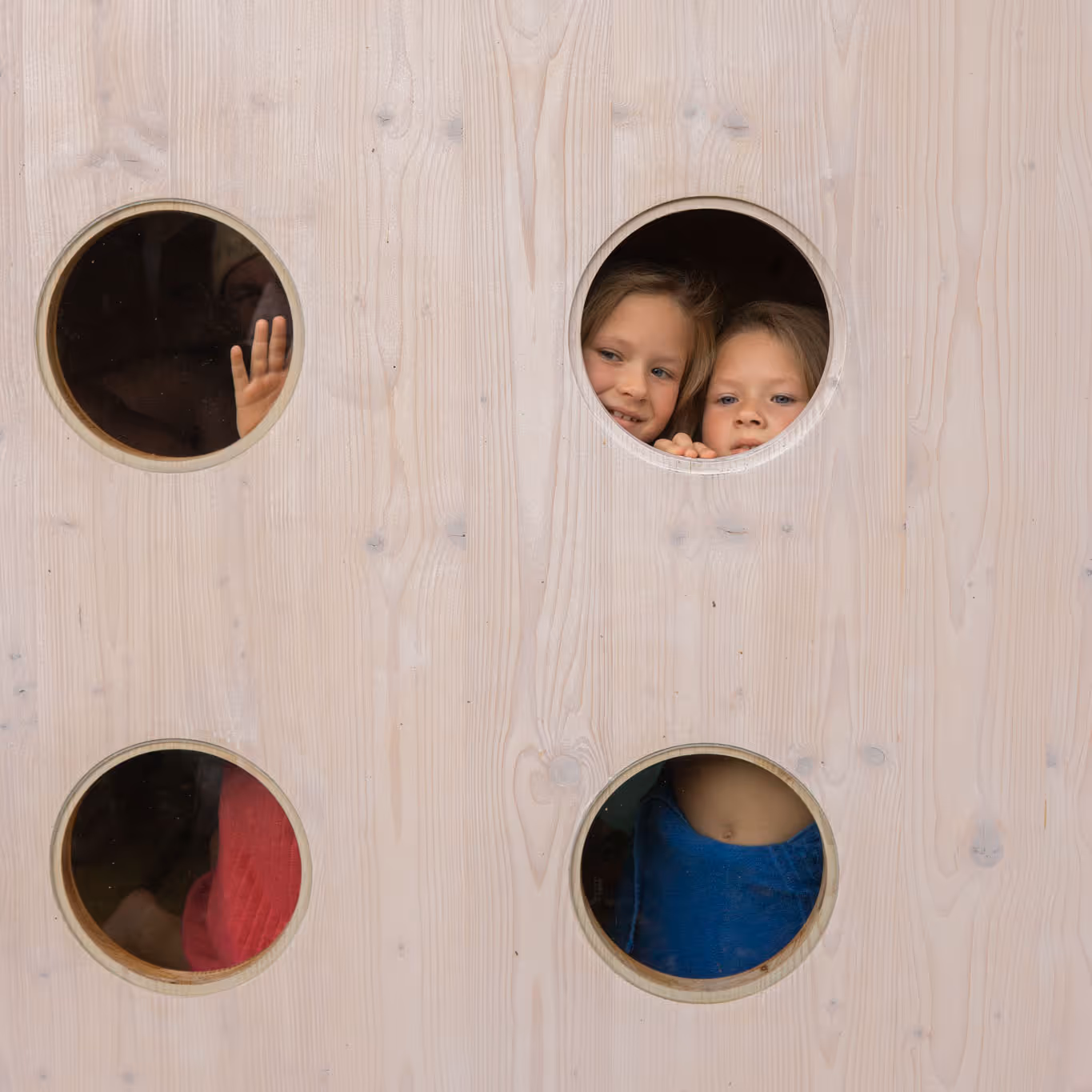 Children waving from the small windows of an outdoor Finnish sauna, captured from the outside.