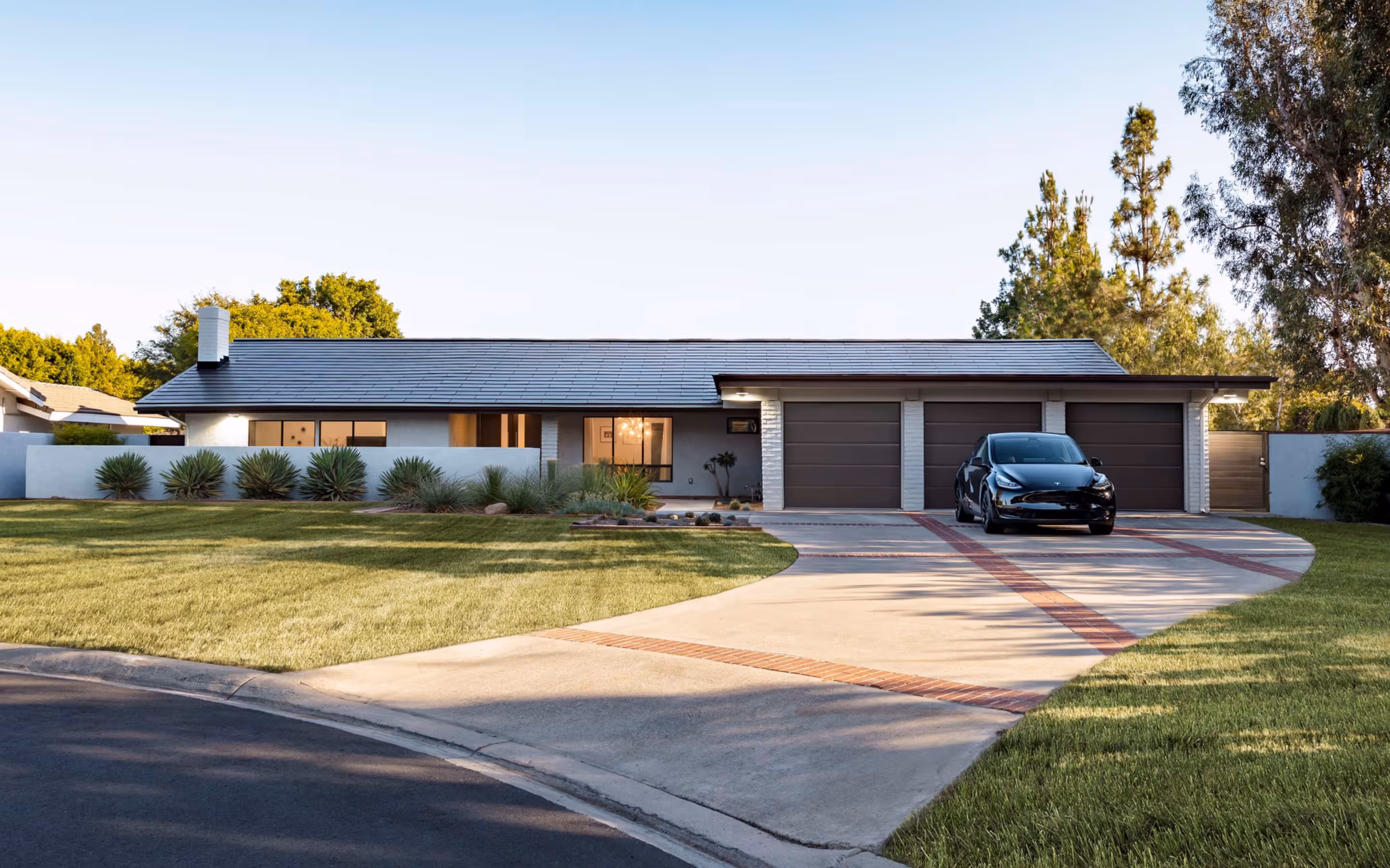 Modern single-story house with dark tiled roof, three-car garage, black car on driveway, and well-maintained lawn.