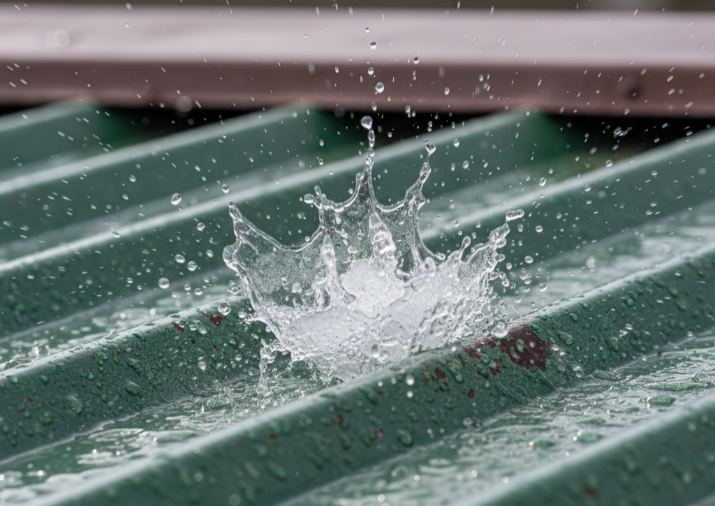 Close-up of a rain droplet splashing on a green corrugated metal surface.