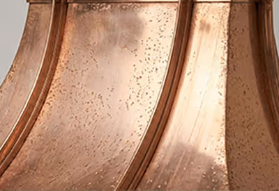 Close-up of a hammered copper metal surface with curved panels and a textured patina.