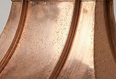 Close-up of a hammered copper metal surface with curved panels and a textured patina.