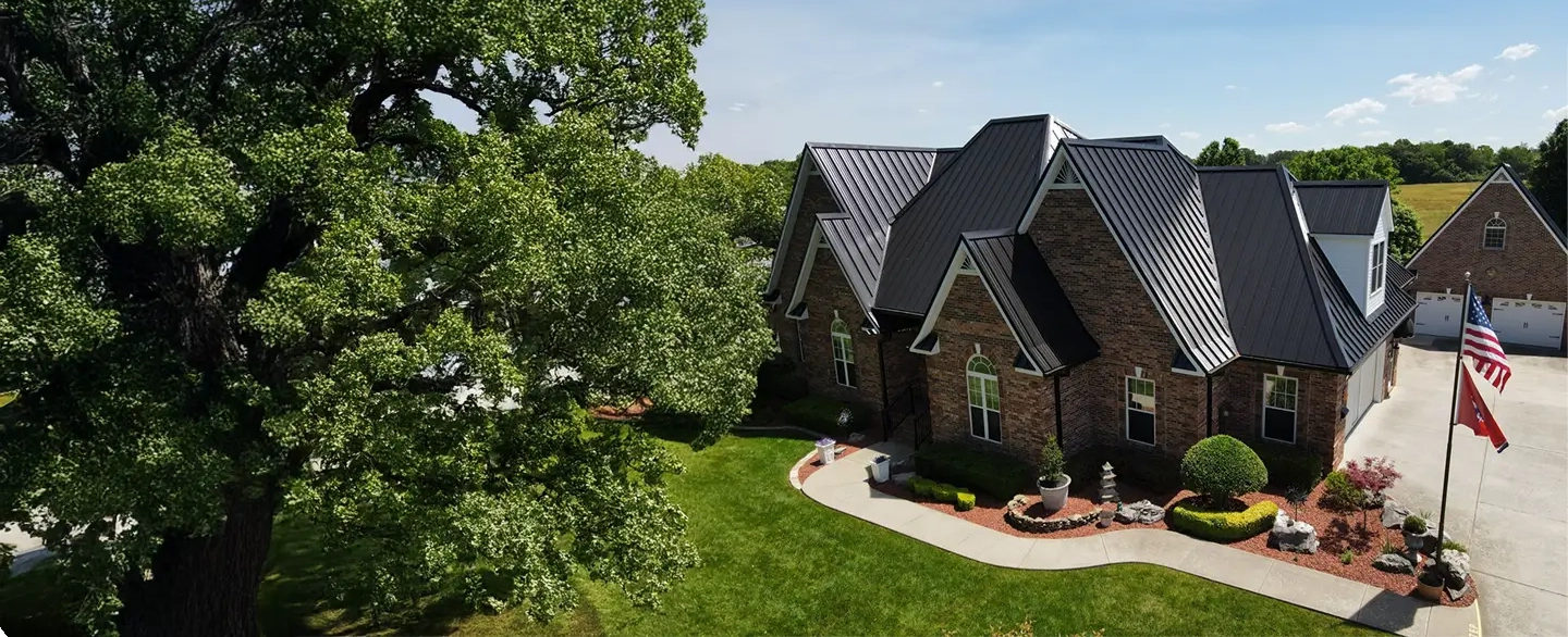 Large brick house with multiple pitched metal roofs, a manicured lawn, and two flagpoles displaying the American and Tennessee flags.