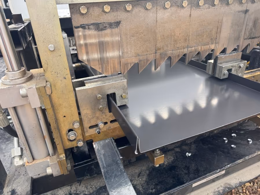 Close-up of a metal press machine with a serrated upper jaw pressing a sheet of metal.