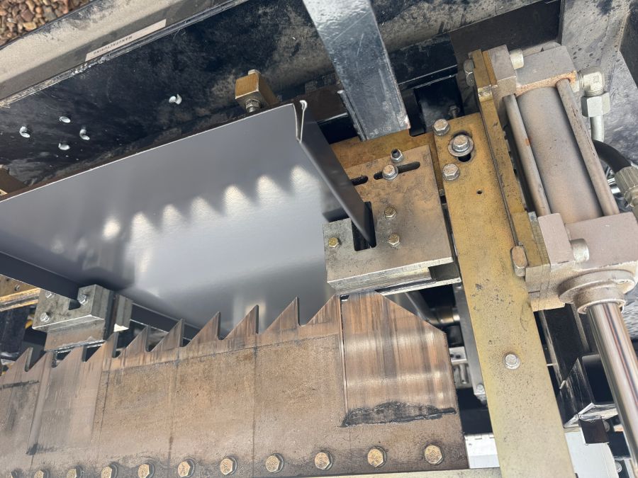 Close-up of a metal press machine with a serrated upper jaw pressing a sheet of metal.