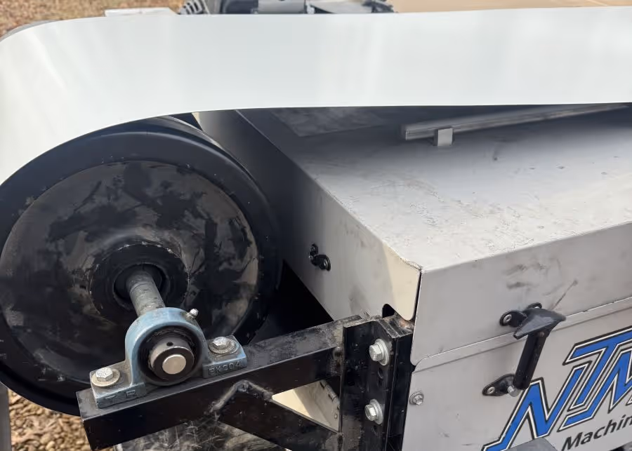 Close-up of a black industrial roller attached to a metal bracket on a silver machine with a partial blue logo.
