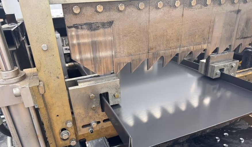 Close-up of a metal sheet being cut by industrial machinery with large serrated blades.