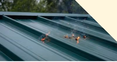 Small flames and smoke burning on a green metal roof panel.