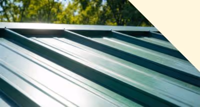 Close-up of a green metal roof panel with trees and blue sky in the background.