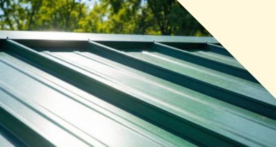Close-up of a green metal roof panel with trees and blue sky in the background.
