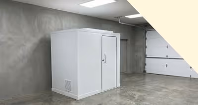 White rectangular soundproof booth placed inside a gray industrial garage with polished concrete floor.