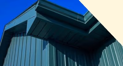 Close-up view of a dark green metal roof edge against a bright blue sky.