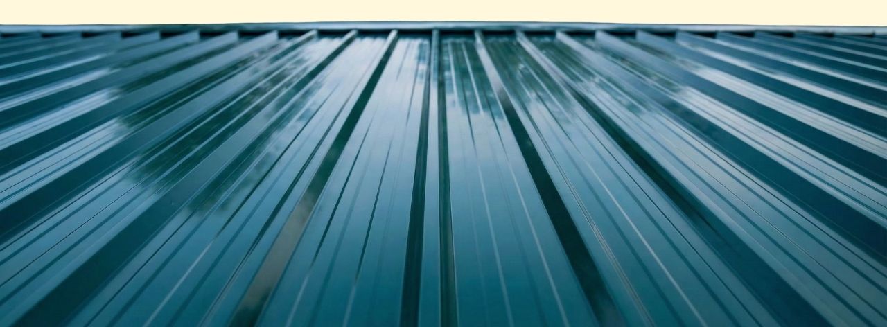 Close-up shot of glossy greenish-blue corrugated metal roof panels with reflections.