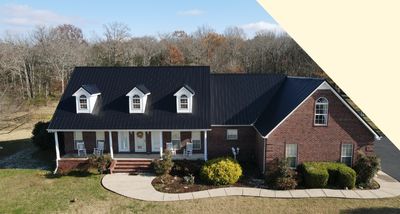 Large two-story brick house with black roof, dormer windows, a front porch, and landscaped bushes.
