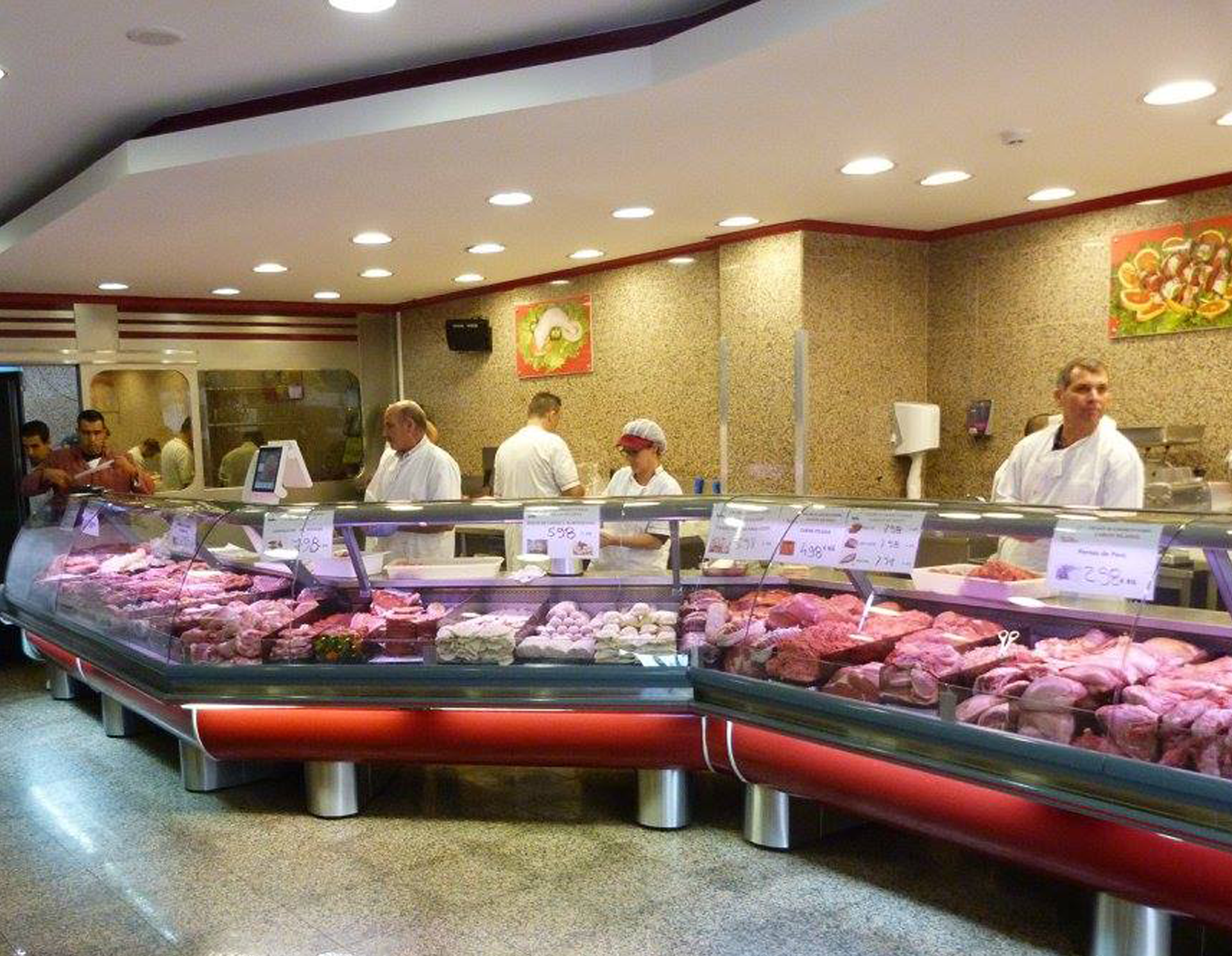 Butcher shop counter displaying various cuts of fresh meat with four staff members behind it in white uniforms.