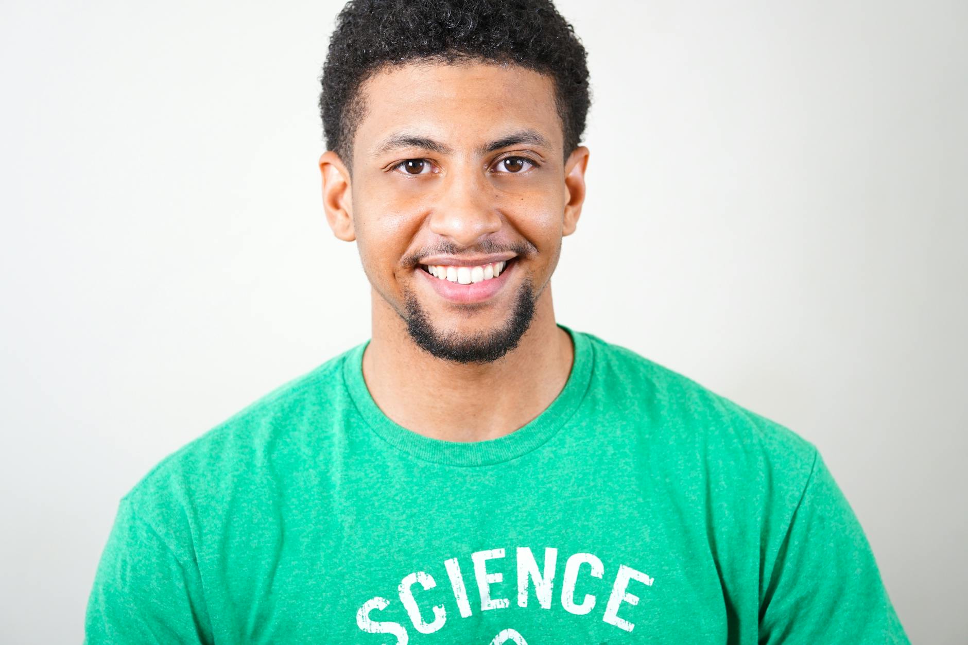 Smiling young man with short curly hair wearing a green shirt with the word 'SCIENCE' in white text.