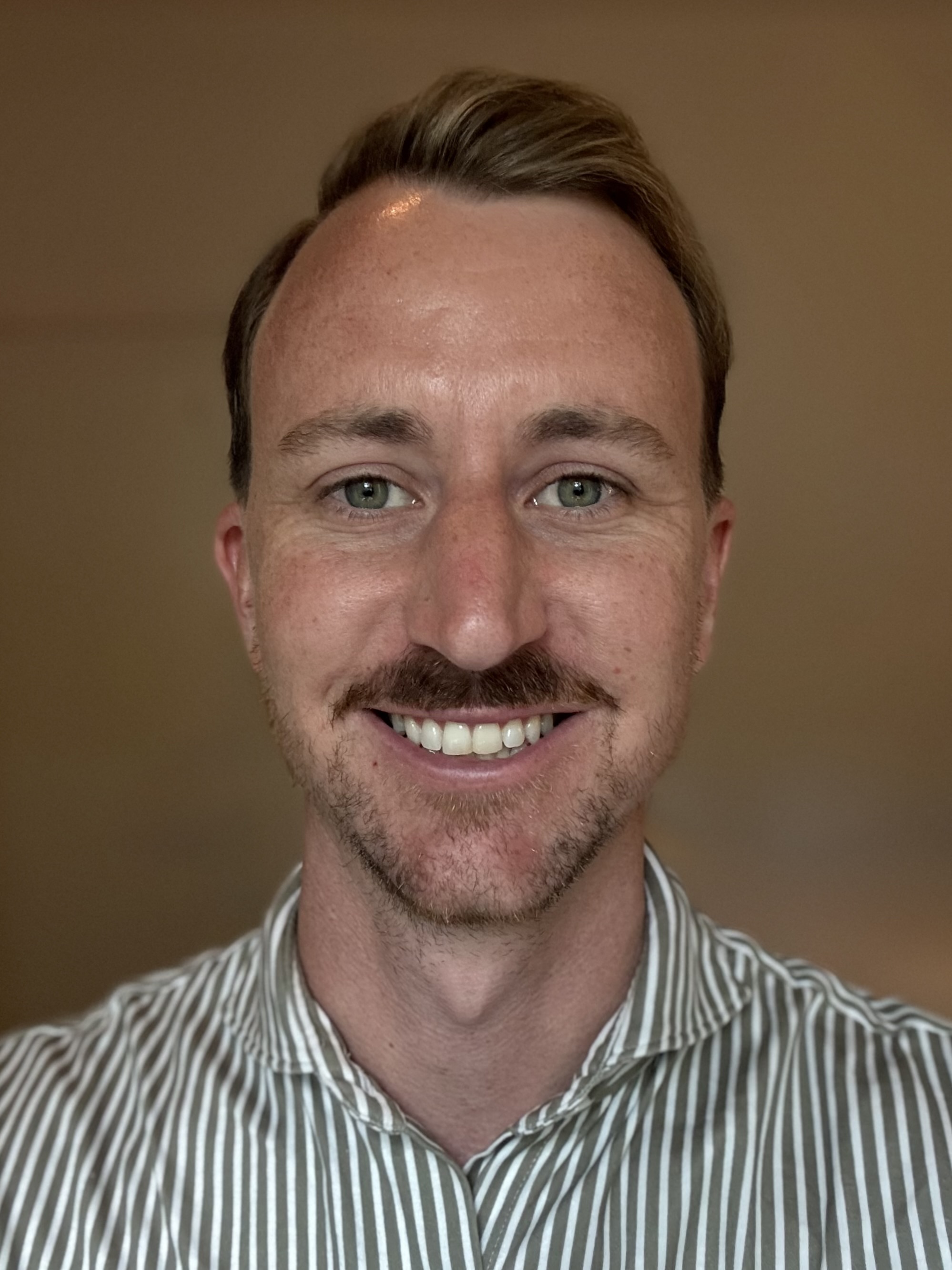 Smiling person in striped shirt against neutral brown background