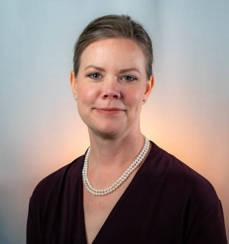 Professional woman in purple sweater wearing pearl necklace, soft background